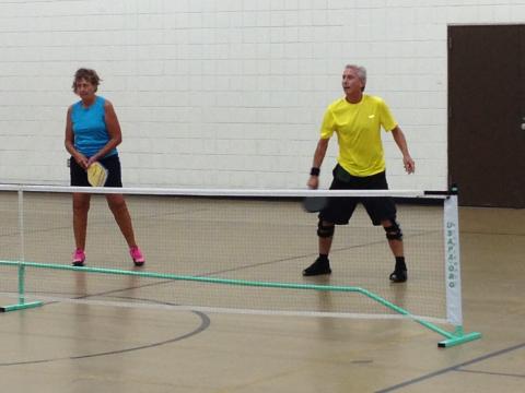 Two adults playing pickleball indoors